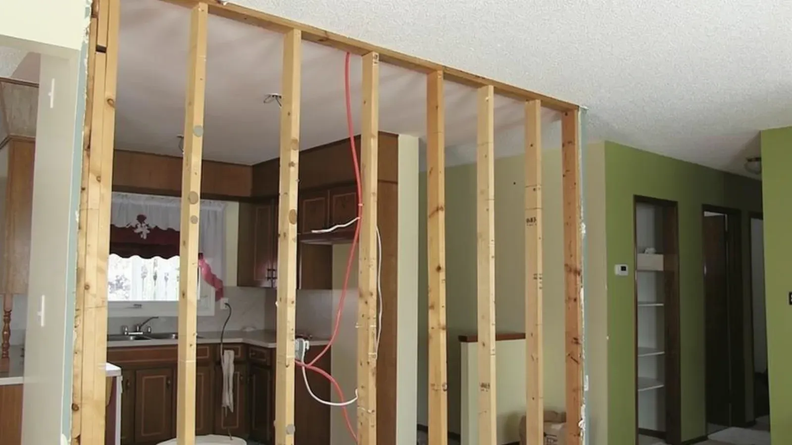 Interior partition wall stripped down to its bare wood stud framing, opening onto the kitchen beyond