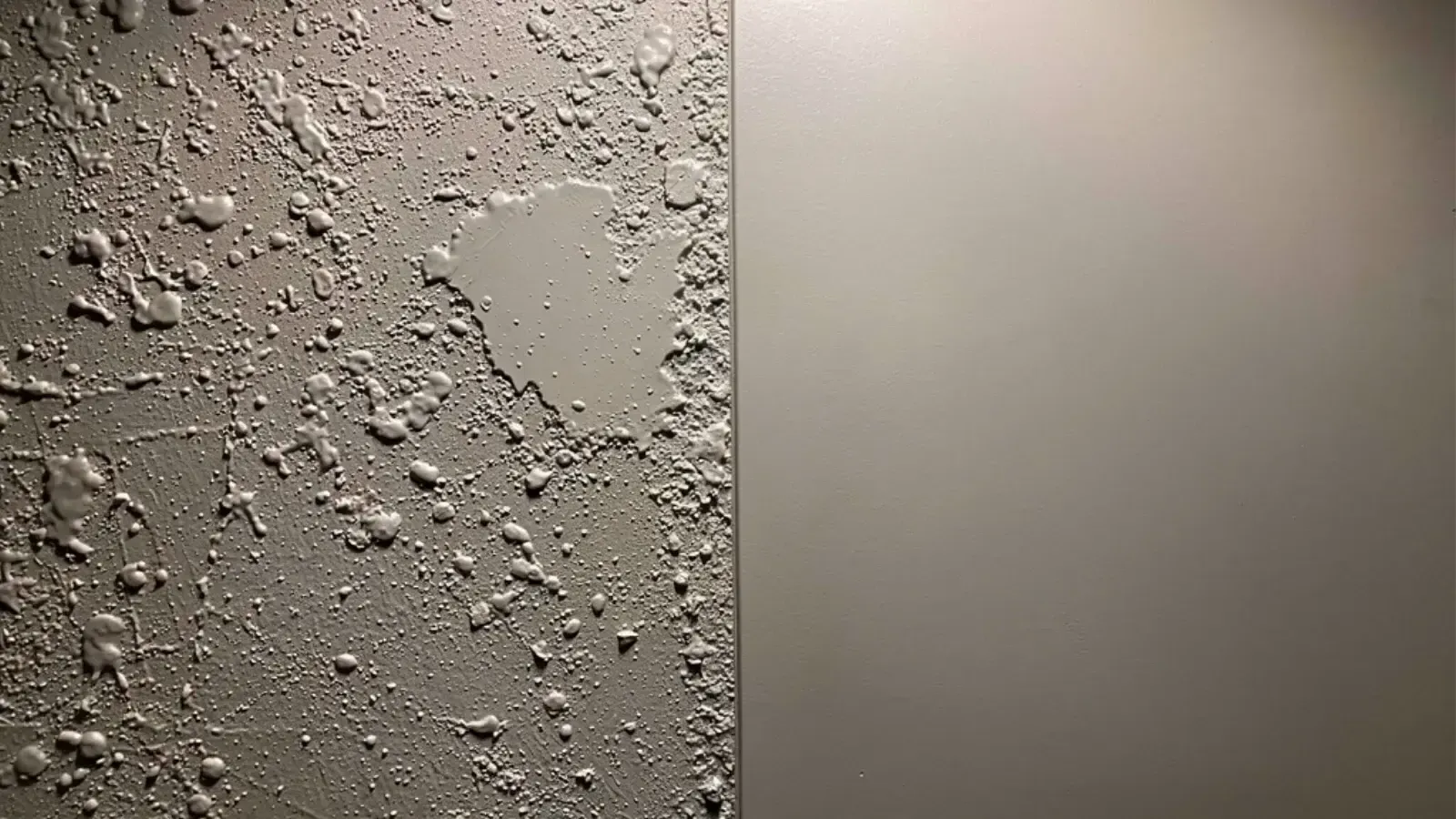 A smooth painted wall meeting a knockdown texture along a vertical line in raking light